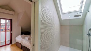 Un dormitorio con cama, tragaluz, ducha y vistas a edificios.