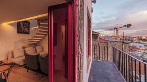 Un balcón con vistas a una obra en construcción, una escalera que sube a un piso superior y un sofá con cojines.