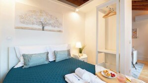 A bedroom with a bed, pillows, a bedside table with a lamp, a painting on the wall, and a tray with food and drinks.