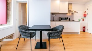 A modern kitchen with white cabinets, a microwave, and a stainless steel range hood. There is a dining table with two chairs and an air conditioning unit above it.
