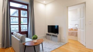 A modern living room with a sofa, a small table with a plant, a TV, and a window with curtains.