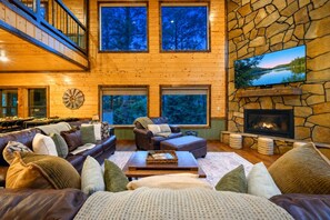 A cozy living room with a fireplace, large windows, and a stone wall.