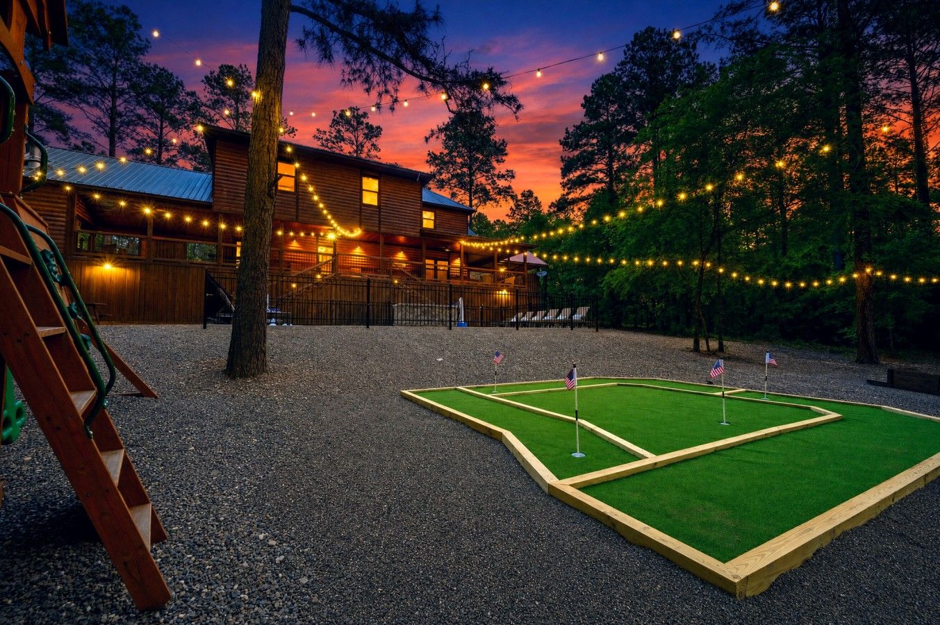 A wooden cabin with a deck, surrounded by trees and string lights.