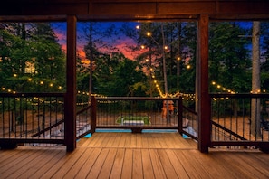 A wooden deck with a railing, string lights, and a view of a playground and trees.