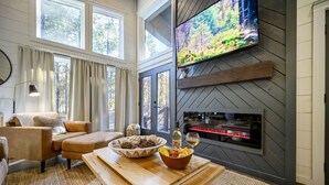 A cozy living room with a fireplace, a television mounted on the wall, and a dining area with a wooden table and chairs.