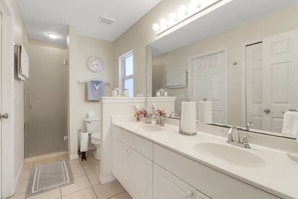 A modern bathroom with a large mirror, dual sinks, and a shower area.