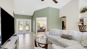A spacious living room with a large flat-screen TV, a glass coffee table, and a beige sofa.