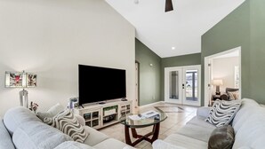A modern living room with a flat-screen TV, a glass coffee table, and a sofa with patterned cushions.