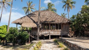 A rustic wooden building with a thatched roof, surrounded by palm trees and tropical vegetation. - 4 bedroom Rote Beach House (Rote Barat)