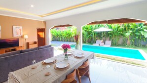 Un salon moderne avec vue sur la piscine, comprenant un canapé, une table à manger et un téléviseur.