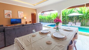 Un salon moderne avec un canapé, une table à manger pour quatre personnes et une vue sur la piscine.