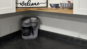 A kitchen with a coffee maker, a 'welcome' sign, and decorative bowls on shelves.