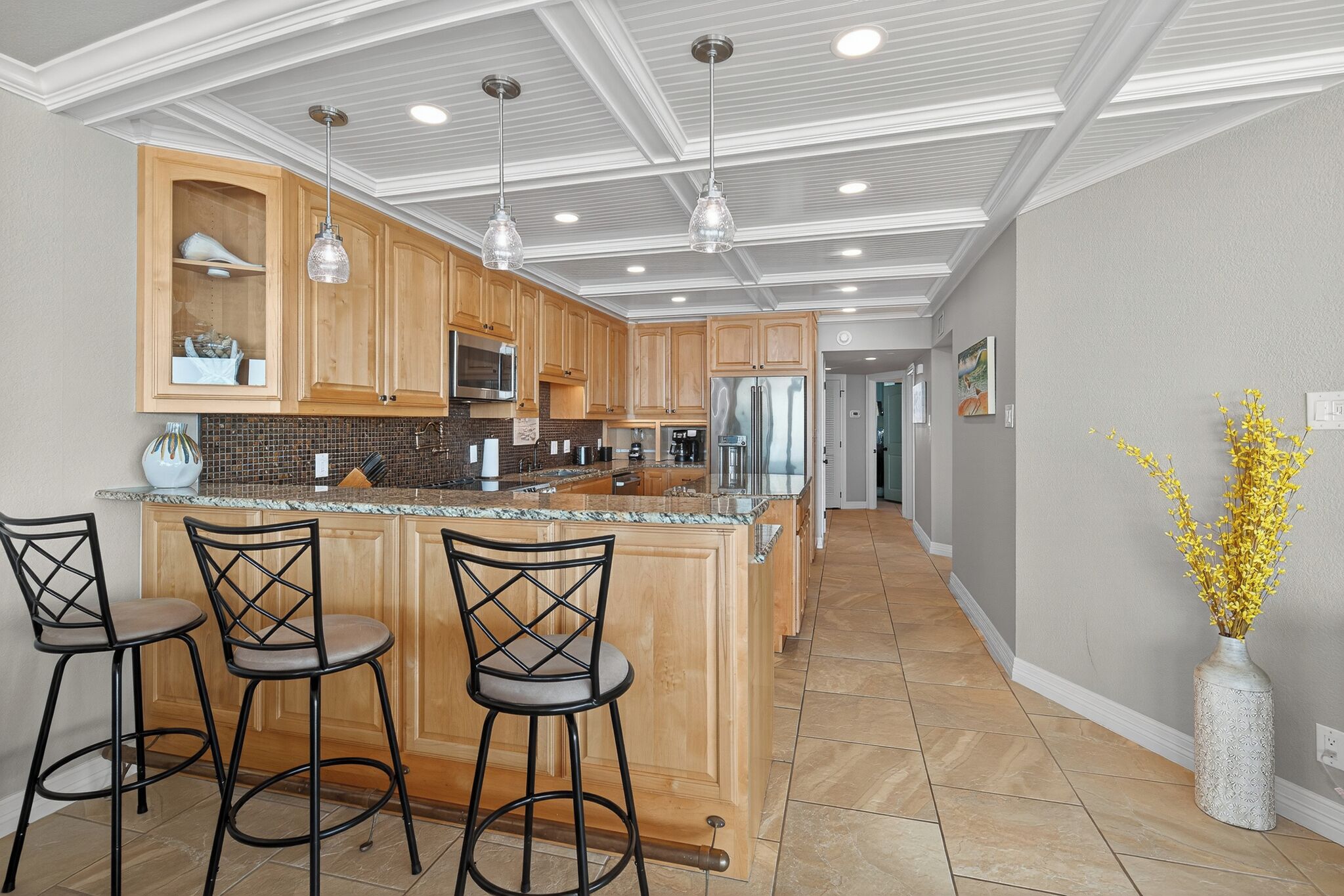 Une cuisine moderne avec des meubles en bois, un îlot central doté de tabourets et des luminaires suspendus.