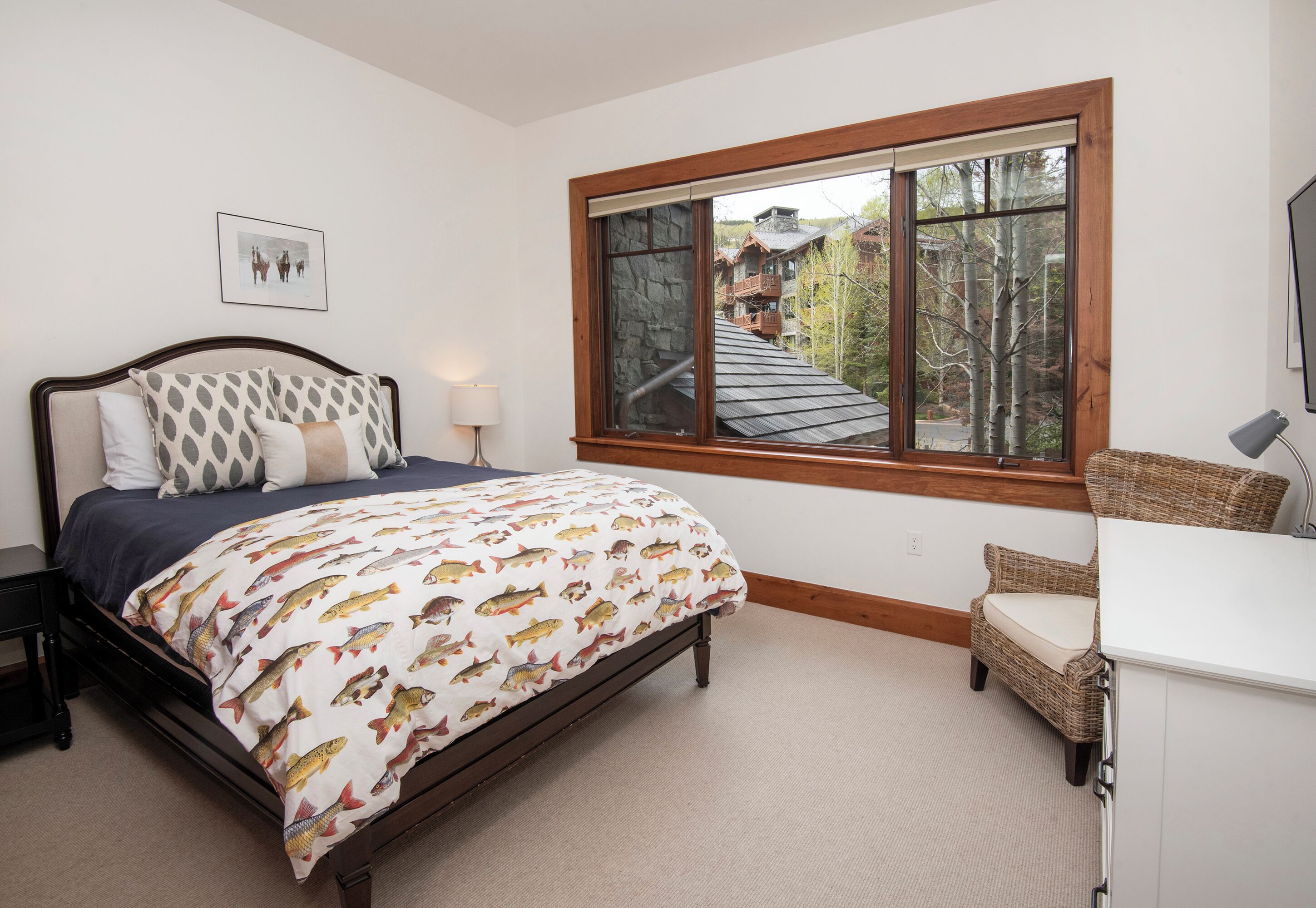 Ein Schlafzimmer mit einem Bett, einem Fenster mit Blick auf ein Gebäude und Bäume, einem Nachttisch und einem Stuhl.