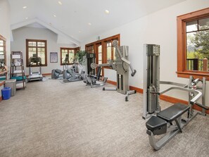 Ein großzügiges Fitnessstudio mit verschiedenen Trainingsgeräten, großen Fenstern und hoher Decke.