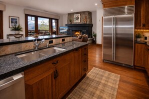 Eine moderne Küche mit Edelstahlkühlschrank, Holzschränken, einer Granit Arbeitsplatte und einem Kamin.