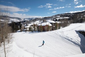 Ein verschneiter Ski-Hang mit einer Person beim Skifahren, umgeben von Gebäuden und Bäumen.