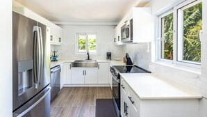 A modern kitchen with white cabinetry, stainless steel appliances, a large window with a view of greenery, and a small mat on the floor.