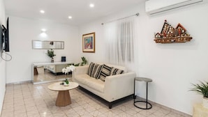 A modern living room with a sofa, a coffee table, a side table, a mirror, a TV, and a decorative wooden shelf.