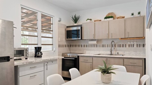 A modern kitchen with white cabinets, a built-in microwave, a stove, and a dining area with a white table and chairs.