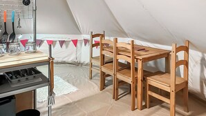 Ein Zeltraum mit Tisch, Stühlen, einer kleinen Küchenzeile und einem weißen Boden.
