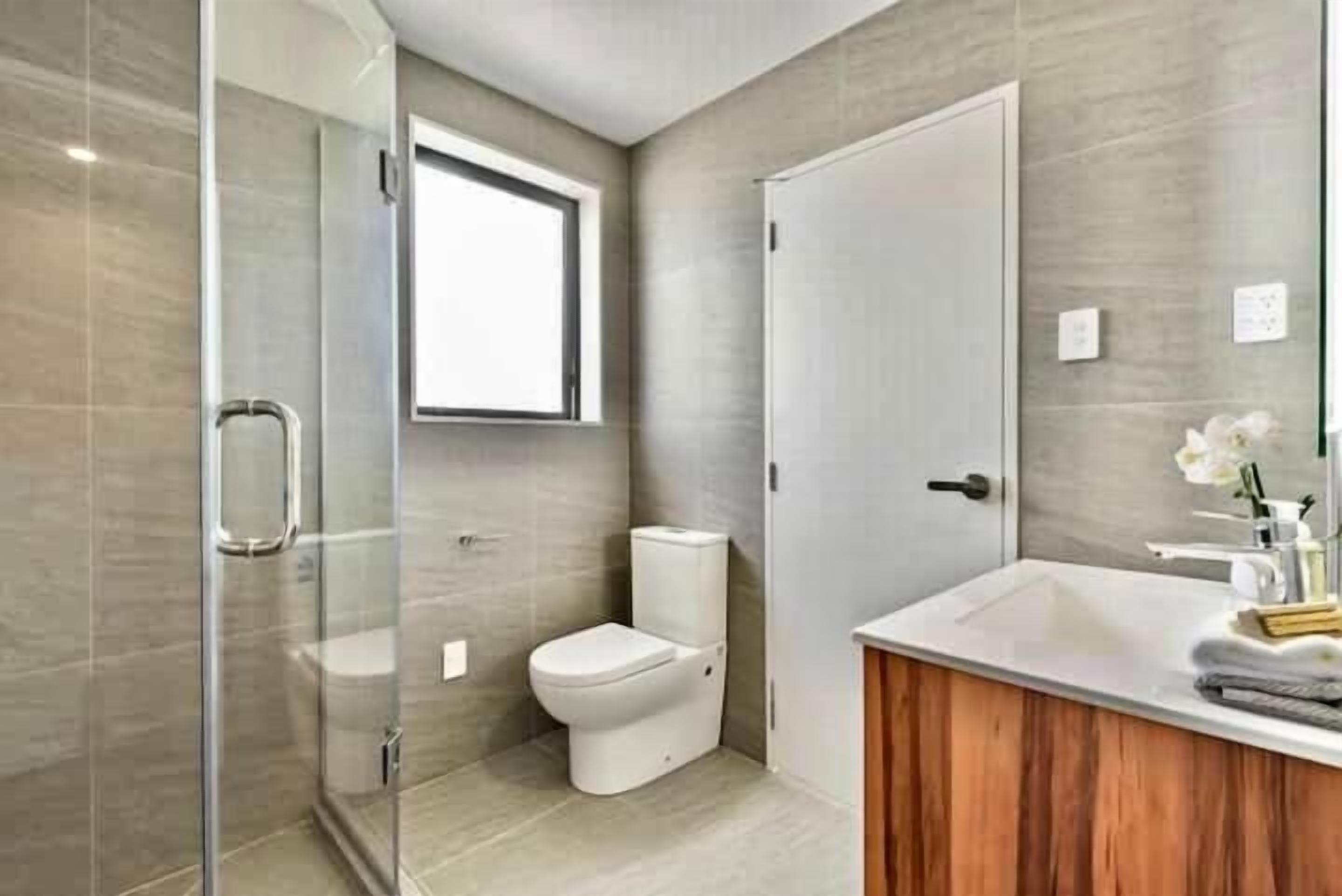 Un baño moderno con cabina de ducha de vidrio, inodoro y lavamanos con tocador de madera.
