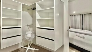 A modern hotel room with a walk-in closet, a bed with a white bedspread, and a standing fan. - Luxury Living in a New Terrace House (Auckland)