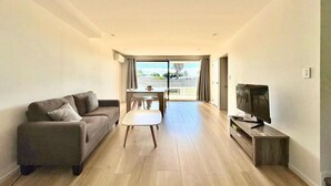 A modern living room with a sofa, a coffee table, a TV, and a dining area with a table and chairs. - Luxury Living in a New Terrace House (Auckland)