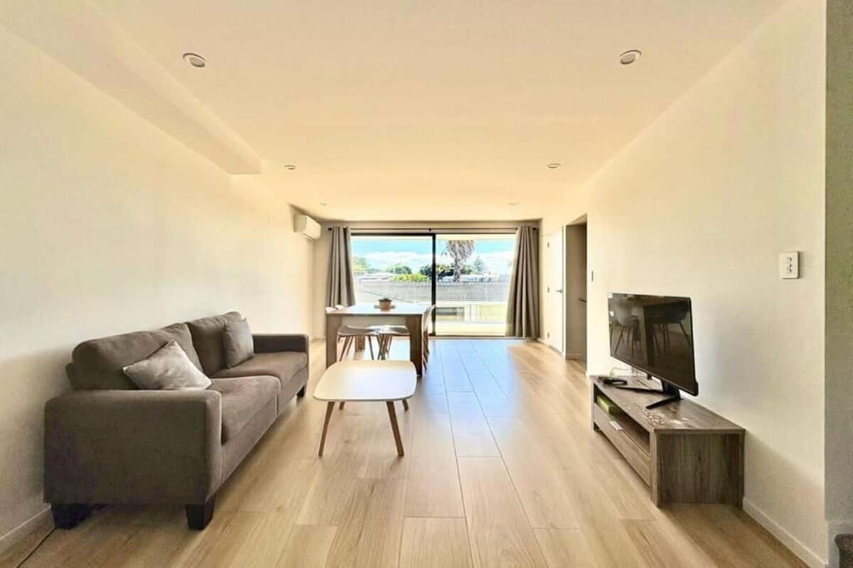 A modern living room with a sofa, a coffee table, a TV, and a dining area with a table and chairs.