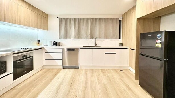 A modern kitchen with white cabinetry, a built-in oven, a dishwasher, and a black refrigerator. - Luxury Living in a New Terrace House (Auckland)