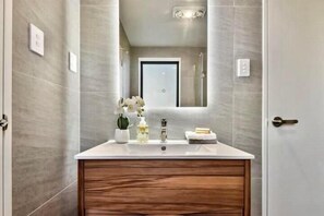 A modern bathroom with a wooden vanity, a large mirror, and a shower area visible through the glass door. - Luxury Living in a New Terrace House (Auckland)
