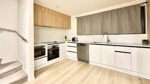 A modern kitchen with white cabinets, a grey backsplash, and a wooden staircase. - Luxury Living in a New Terrace House (Auckland)