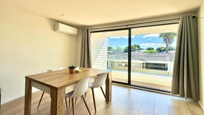 A modern room with a wooden dining table, two chairs, and a large sliding glass door leading to a balcony with a view of a residential area. - Luxury Living in a New Terrace House (Auckland)