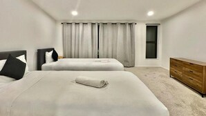 A hotel room with two beds, a wooden dresser, and a window with curtains. - Luxury Living in a New Terrace House (Auckland)