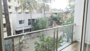 A view from a balcony with a metal railing, overlooking a street with buildings and palm trees.