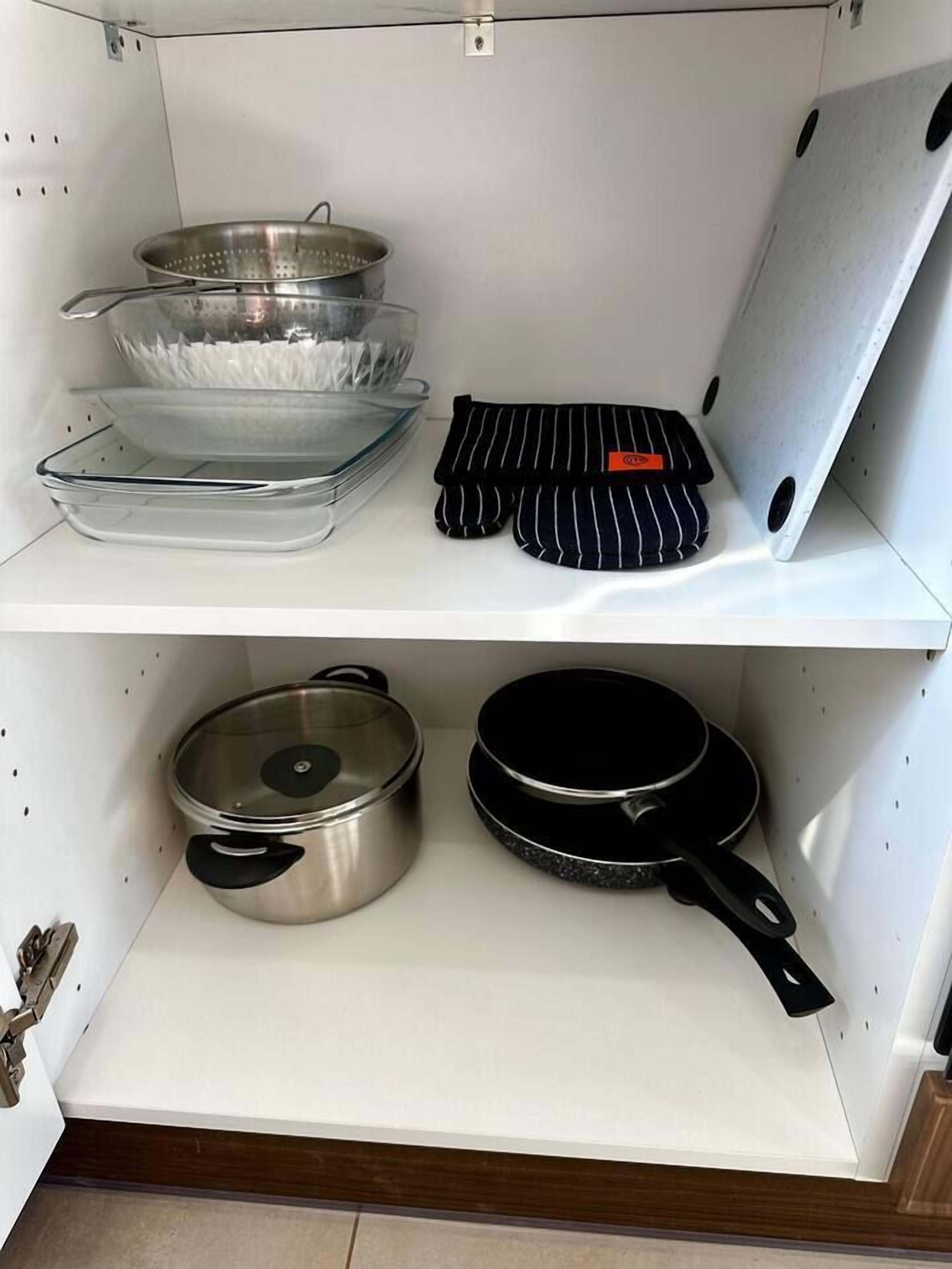 Een keuken met roestvrijstalen kookgerei, waaronder een pan en een koekenpan, en een vergiet op de bovenste plank.
