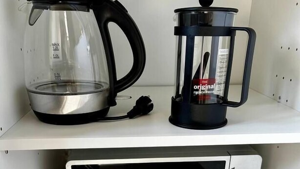 A kitchen with a coffee maker, a French press, and a microwave.