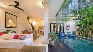 A modern living room with a white sofa, a ceiling fan, and a dining area with wooden furniture. - Villa Mandari (Seminyak)
