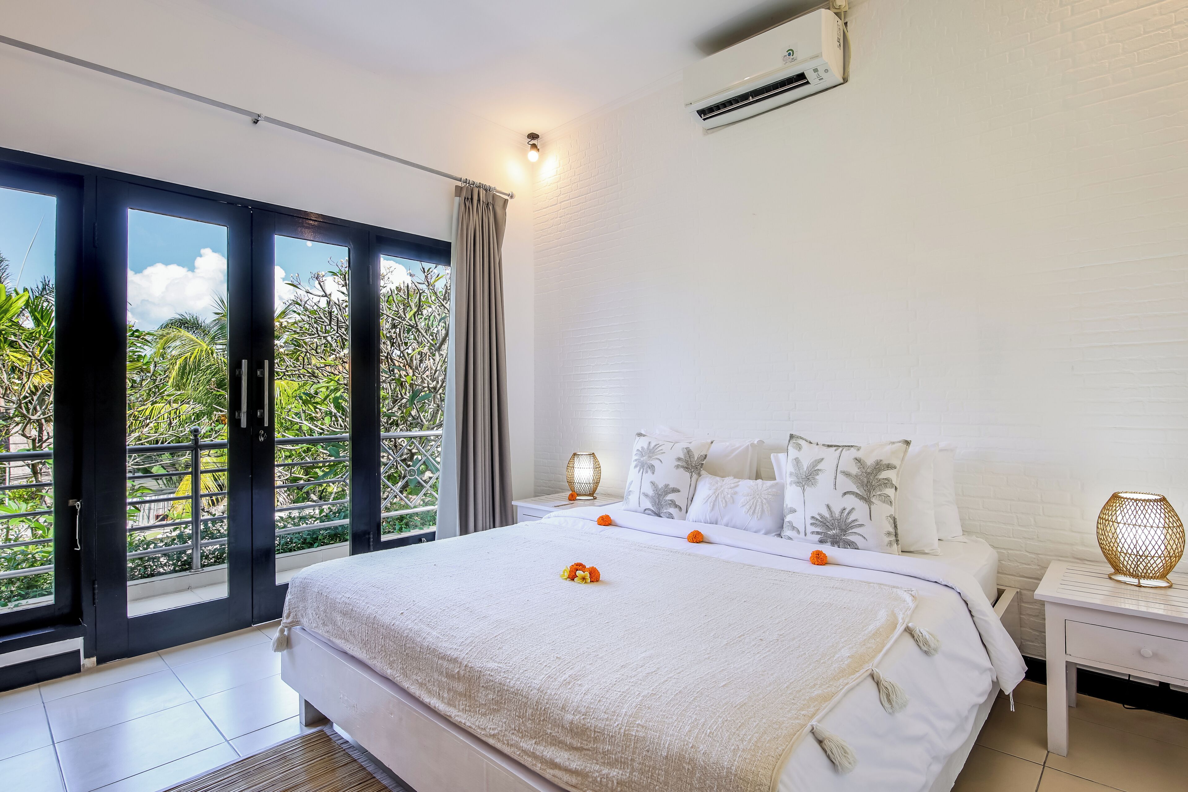 A bedroom with a large bed, a nightstand, a lamp, and a view of greenery through the sliding doors.