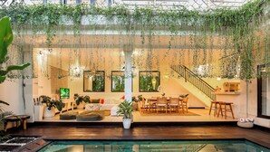 An indoor swimming pool area with a staircase, seating area, and hanging plants. - Villa Mandari (Seminyak)