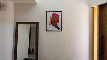 Un pasillo con un espejo grande, una obra de arte enmarcada y un par de zapatos en el suelo.