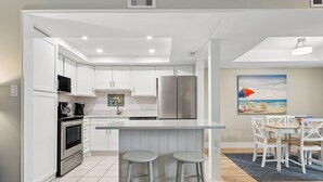 Una cucina moderna con mobili bianchi, elettrodomestici in acciaio inossidabile e un'area bar con sgabelli.