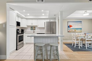 A modern kitchen with white cabinets, stainless steel appliances, and a bar area with stools.
