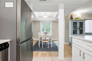 A modern kitchen with a stainless steel refrigerator, a dining table with chairs, and a light blue cabinet with a plant on top.
