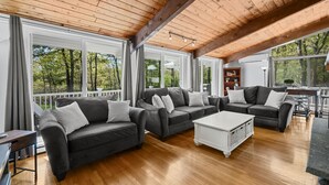 A spacious living area with wooden flooring, large windows offering a view of trees, and a modern fireplace. - Relax at This Dog-Friendly Sandwich Retreat (Sandwich)