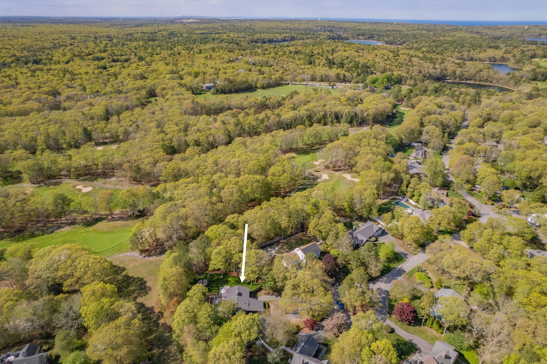 An aerial view of a residential area with houses, a golf course, and a lake.