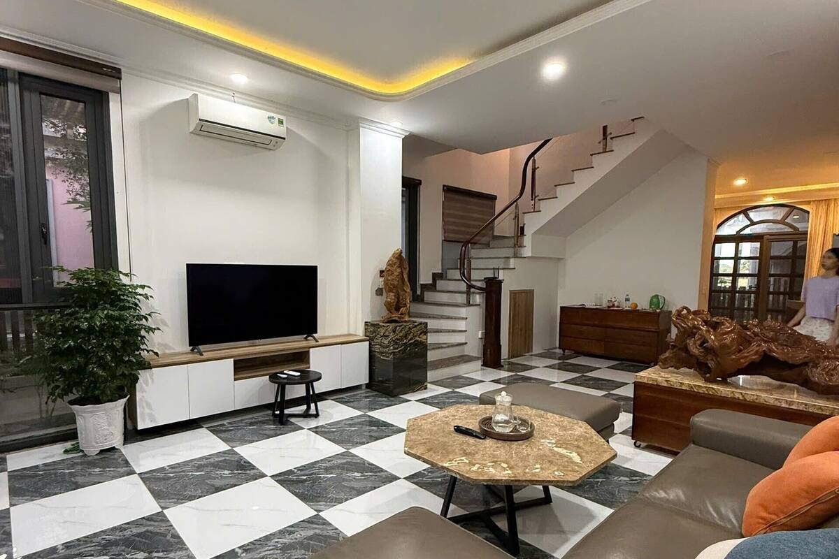 A modern living room with a checkered floor, a flat-screen TV, a sofa, and a staircase leading to another level.