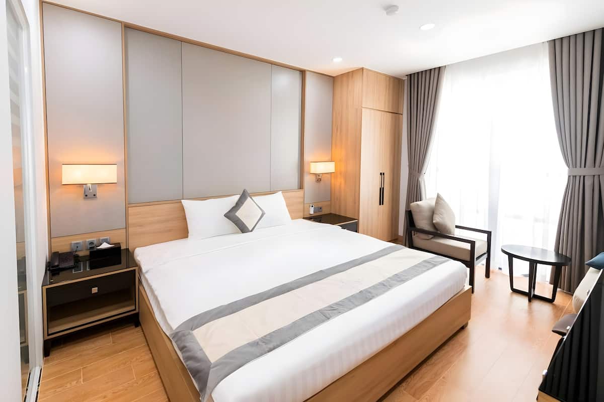 A modern hotel room with a large bed, bedside lamps, a small table, and a chair.