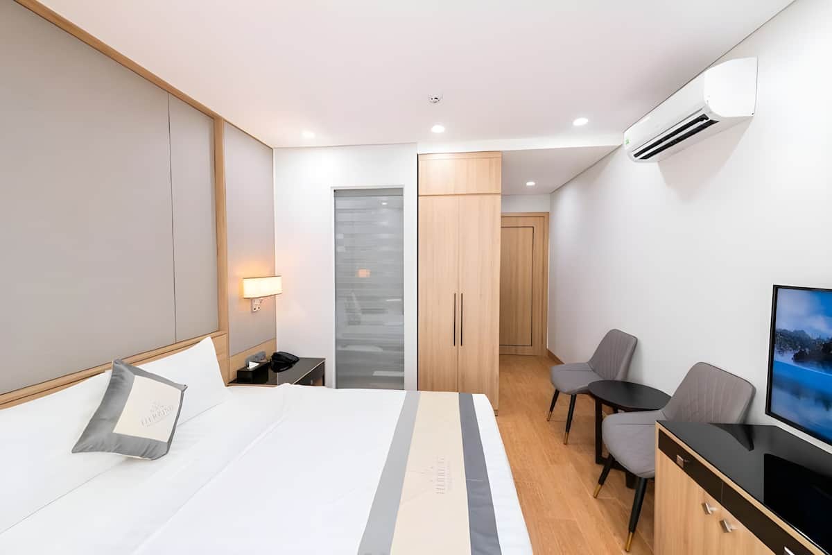 A modern hotel room with a bed, a desk, a chair, a TV, and an air conditioning unit.