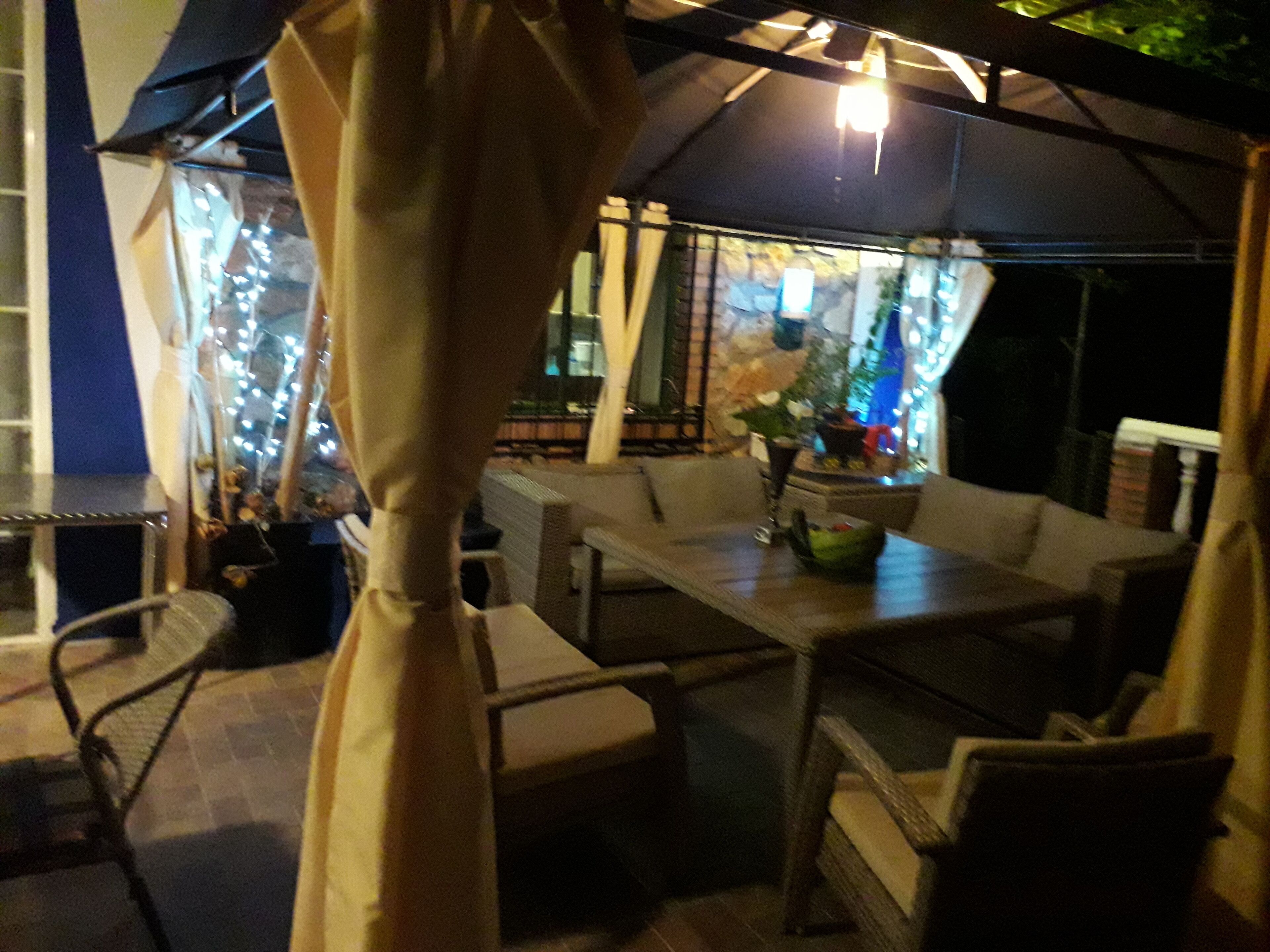 Un espace extérieur aménagé en terrasse, avec une table et des chaises, un luminaire suspendu et une vue sur la rue.